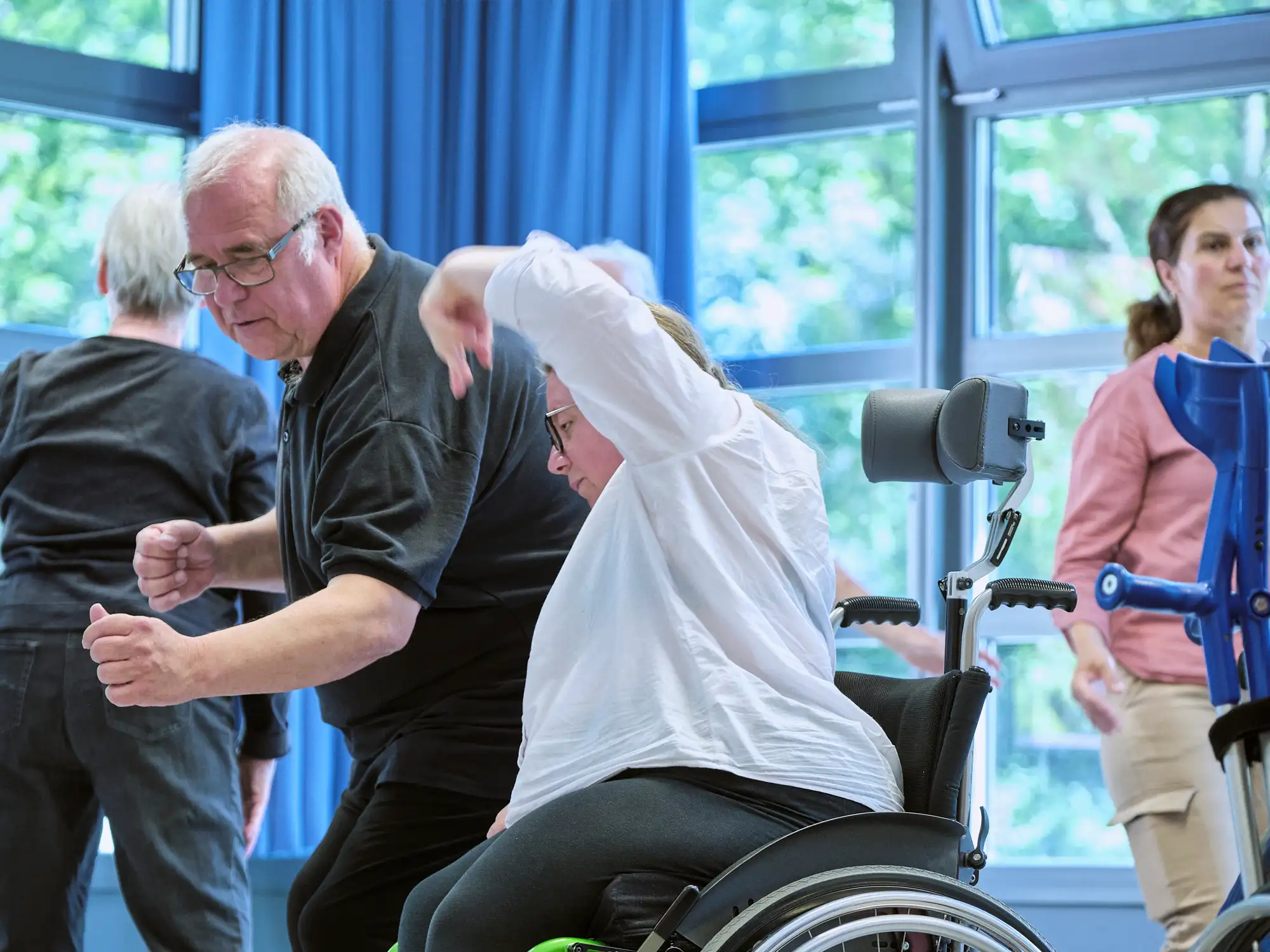 Ein Mann tanzt mit einer Frau in einem Rollstuhl. Sie bewegen ihre Arme und Oberkörper zueinander.