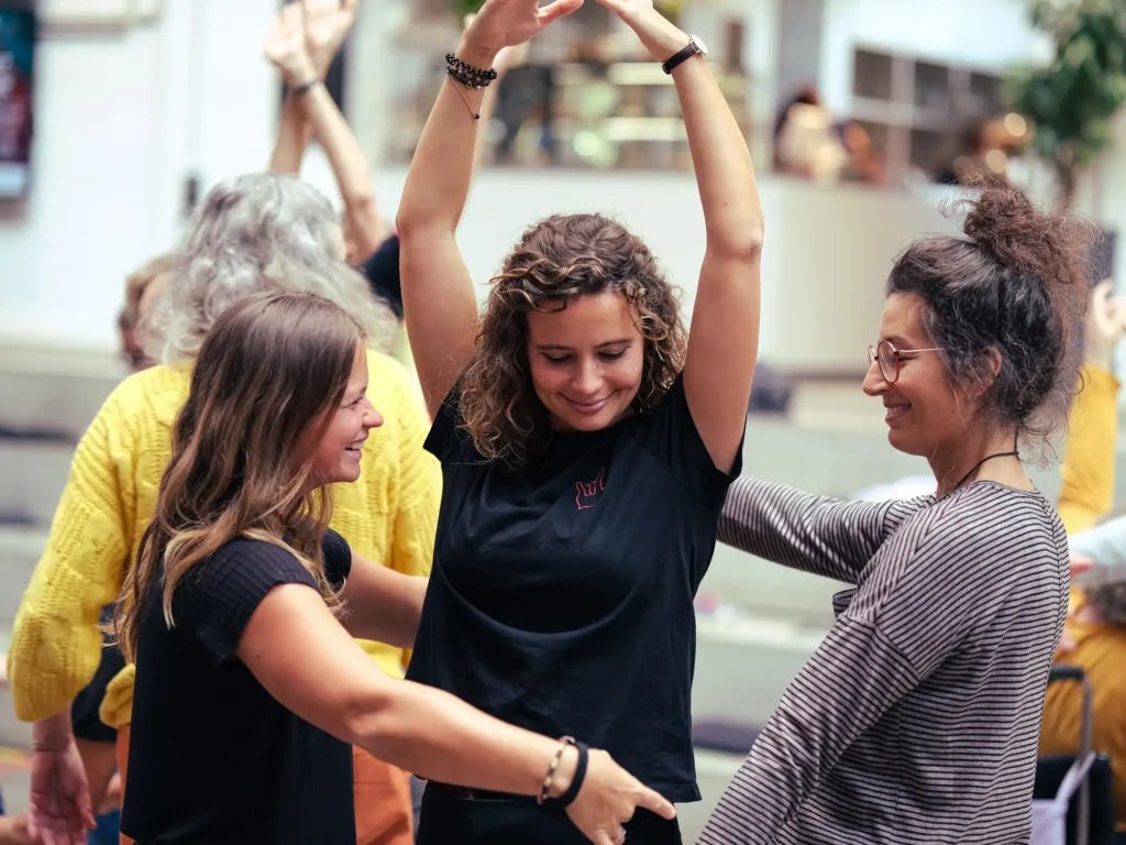 Eine Frau tanzt mit erhobenen Armen zwischen zwei anderen Tänzerinnen