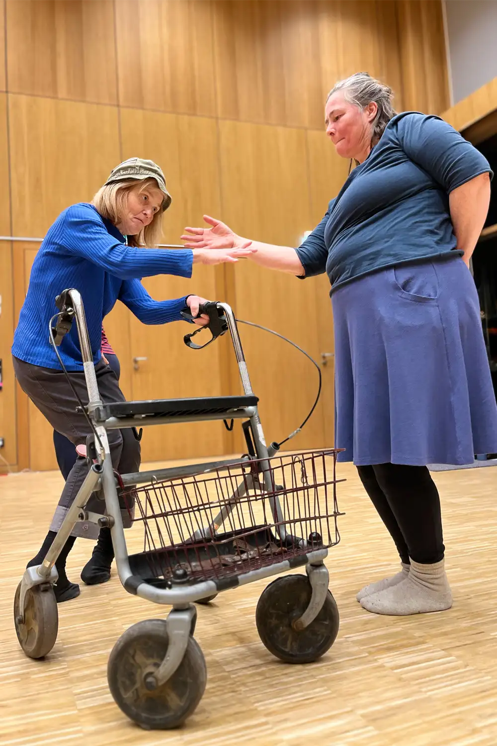 Eine tanzende Person mit einem Rollator streckt ihren Arm einer anderen Person entgegen.